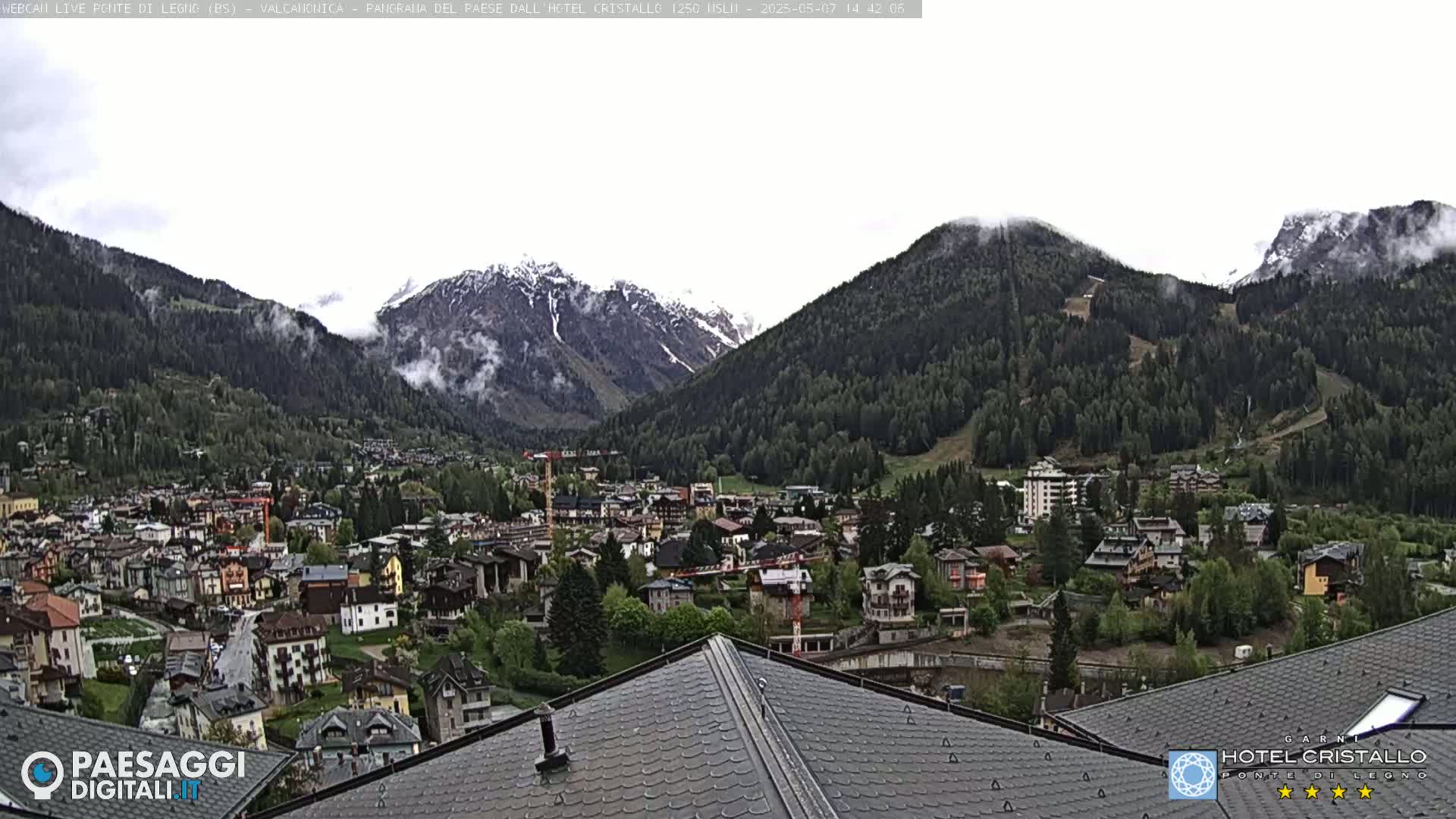 A mountain town nestled in a valley, partially obscured by clouds, with snow-capped mountains in the background.
