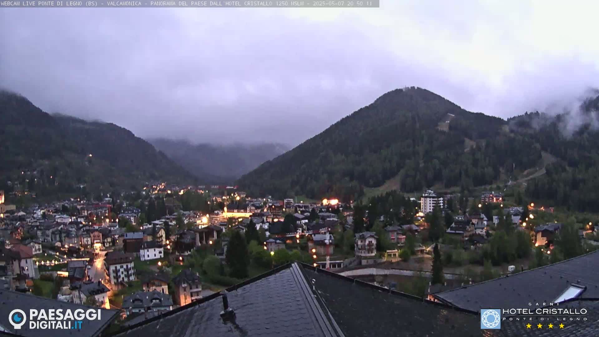A nighttime view of a town nestled in a valley between mountains, under an overcast sky.
