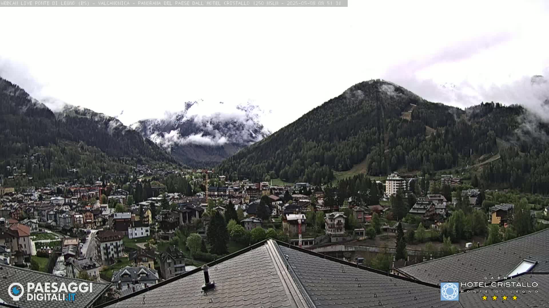 A mountain town nestled in a valley between partially cloudy mountains, viewed from a rooftop.