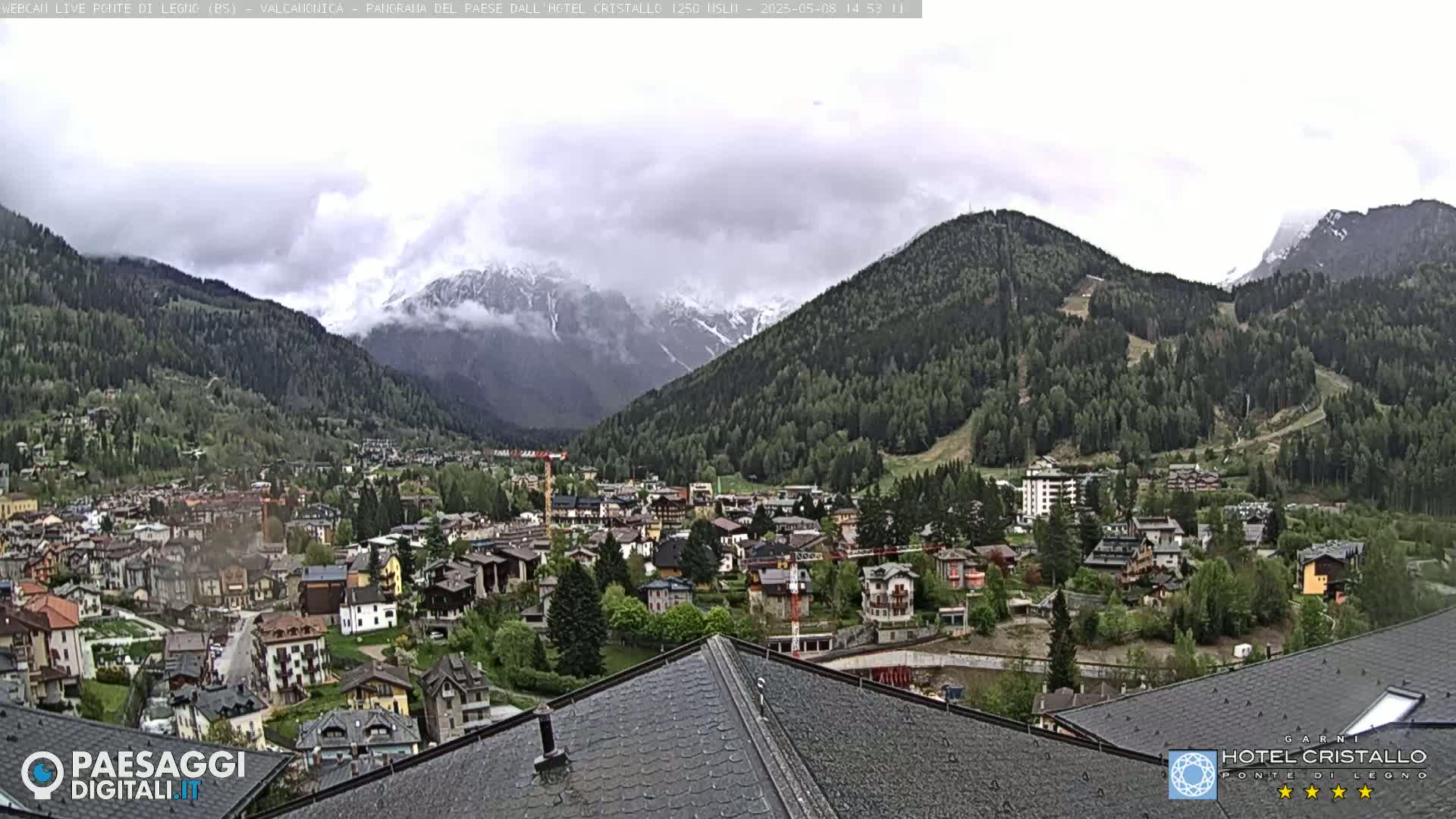 A mountain town nestled in a valley between snow-capped mountains under an overcast sky.