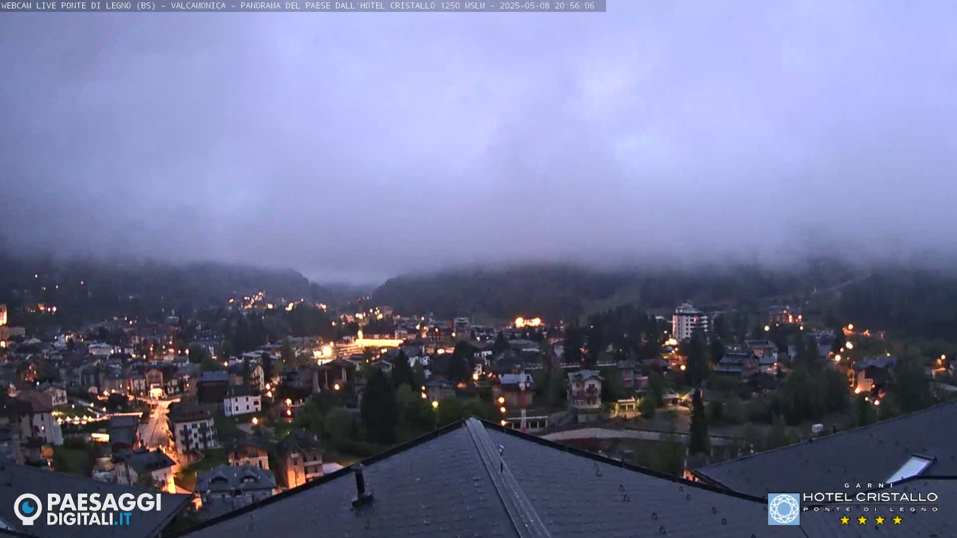 A nighttime view of a town nestled in a valley shrouded in fog, with lights illuminating the buildings below.