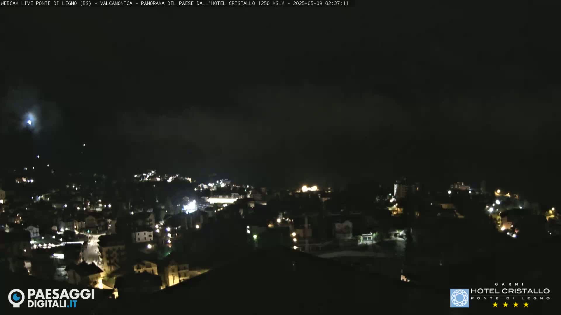 A nighttime, dimly lit town is visible under a dark, cloudy sky.