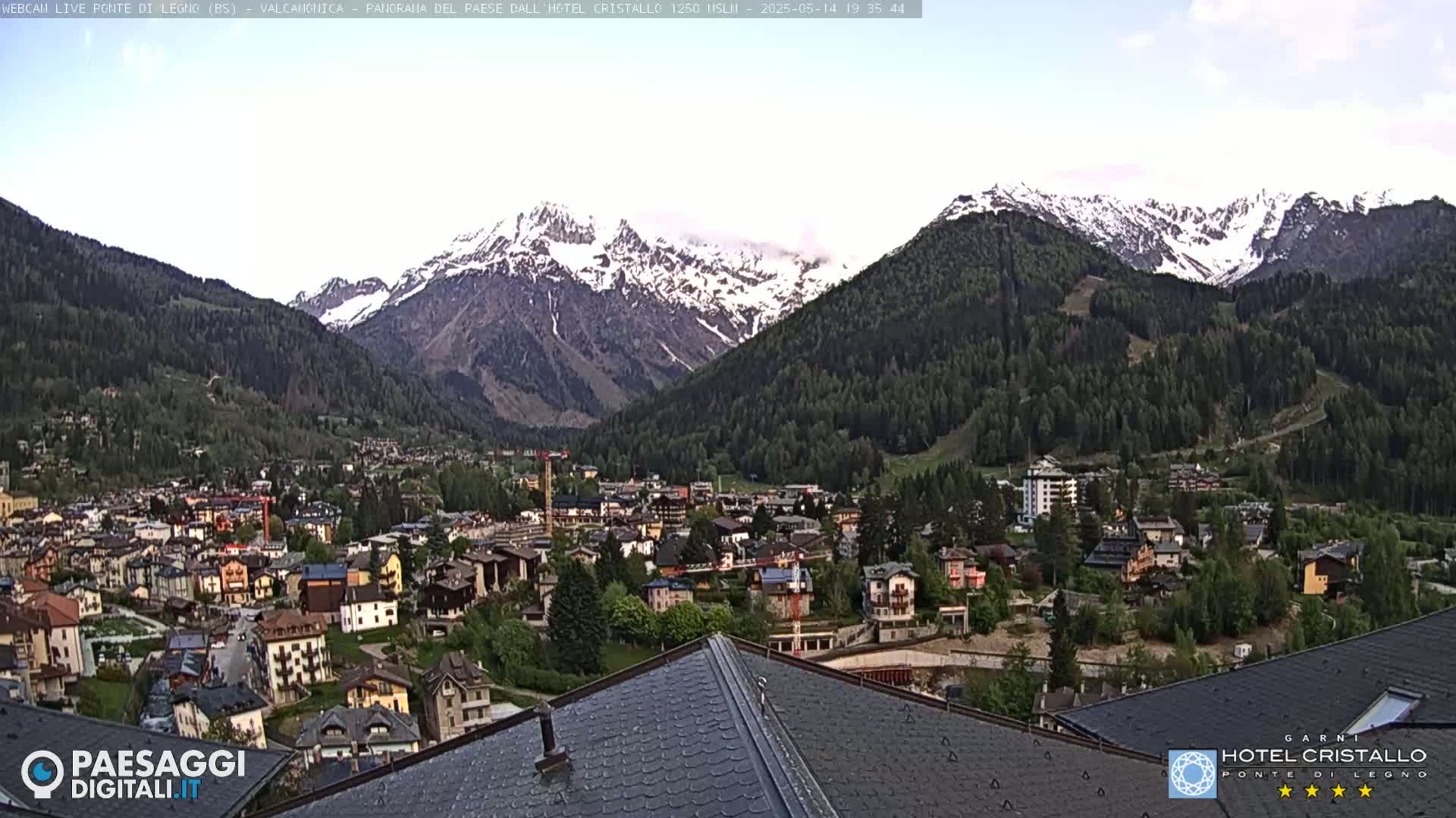 A mountain town nestled in a valley, surrounded by snow-capped mountains under a partly cloudy sky.