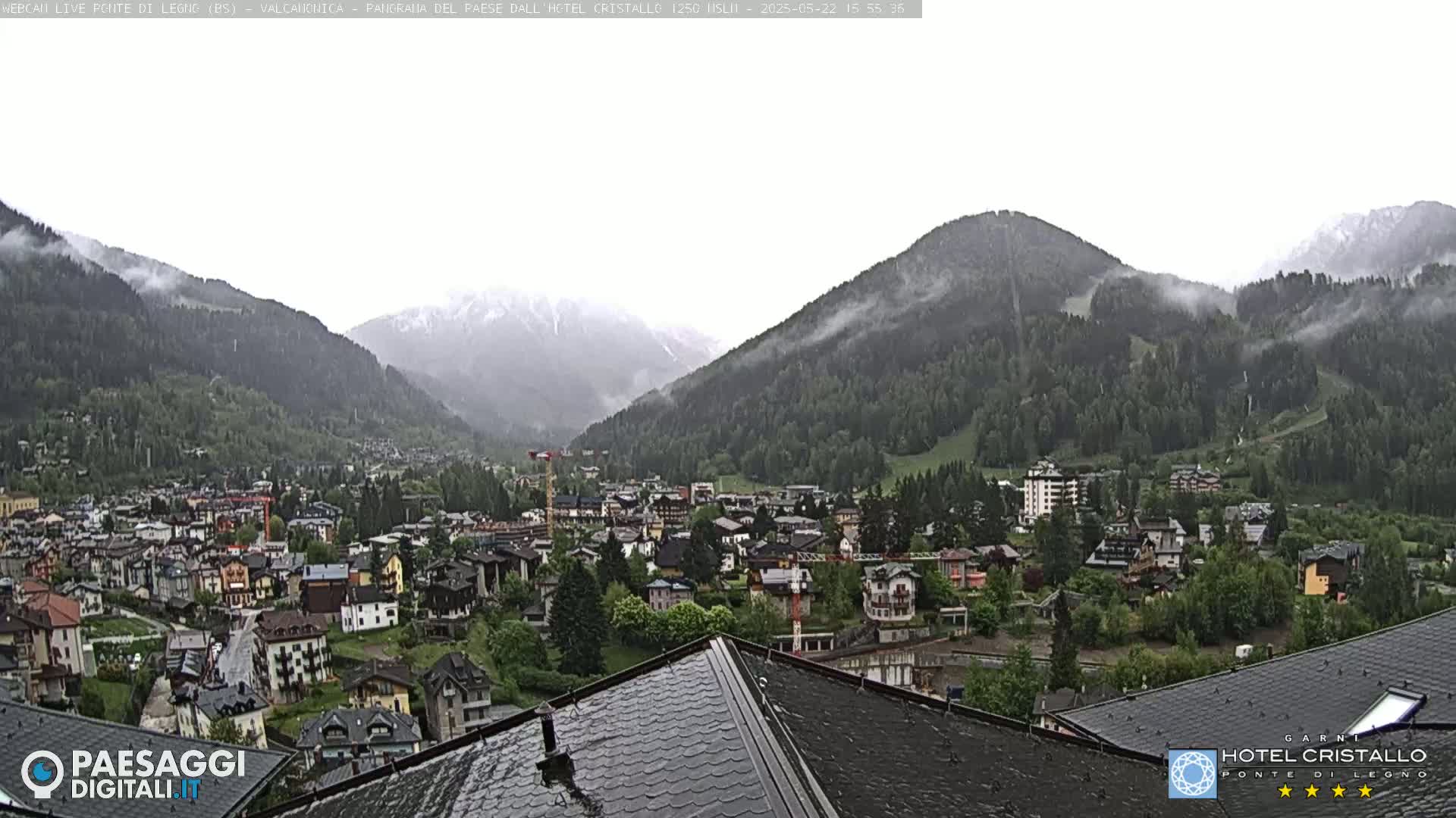 A misty mountain valley town is viewed from a rooftop, with rain falling on dark grey slate tiles.