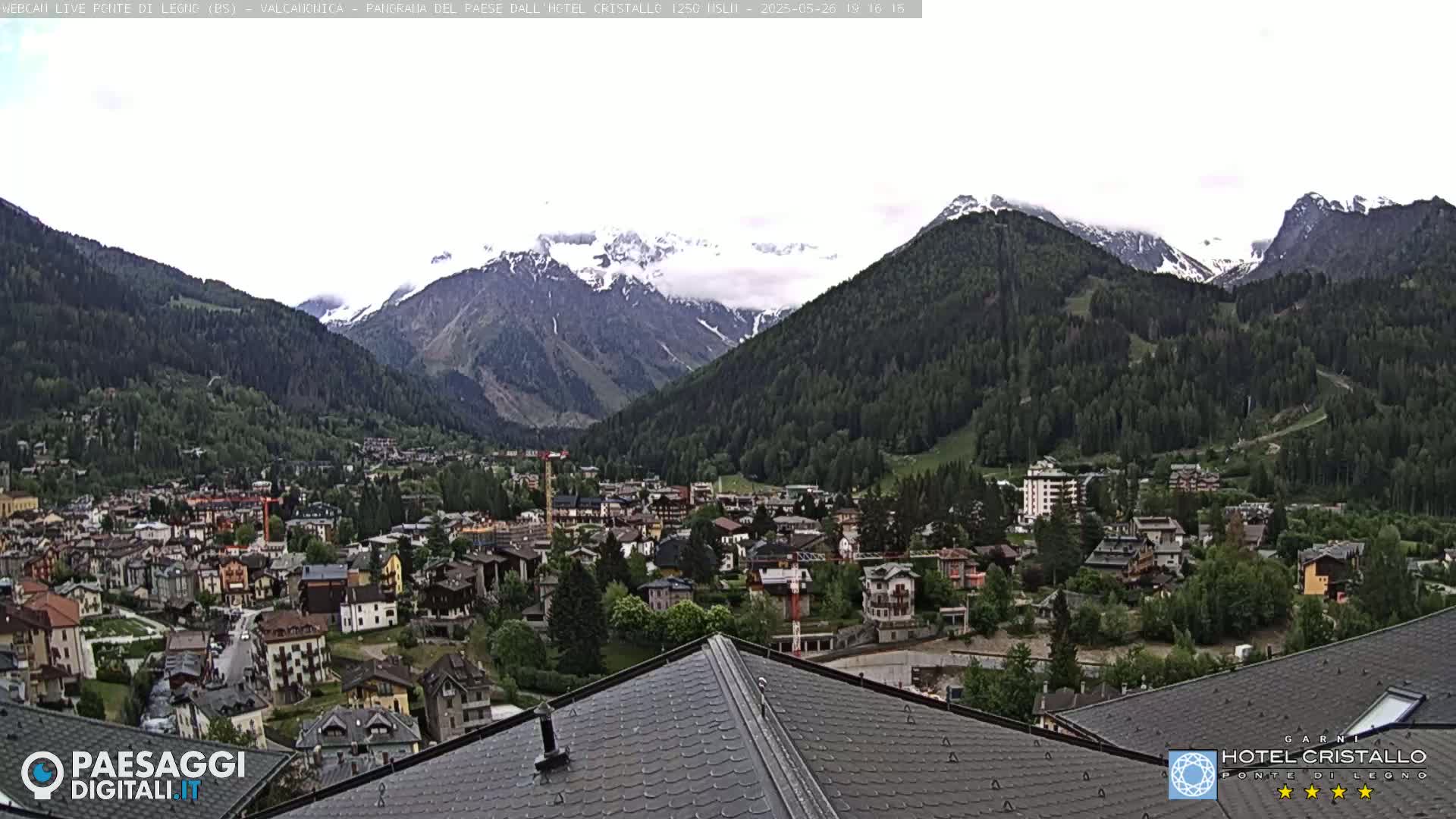 A mountain town nestled in a valley, partially clouded, with snow-capped mountains in the background.