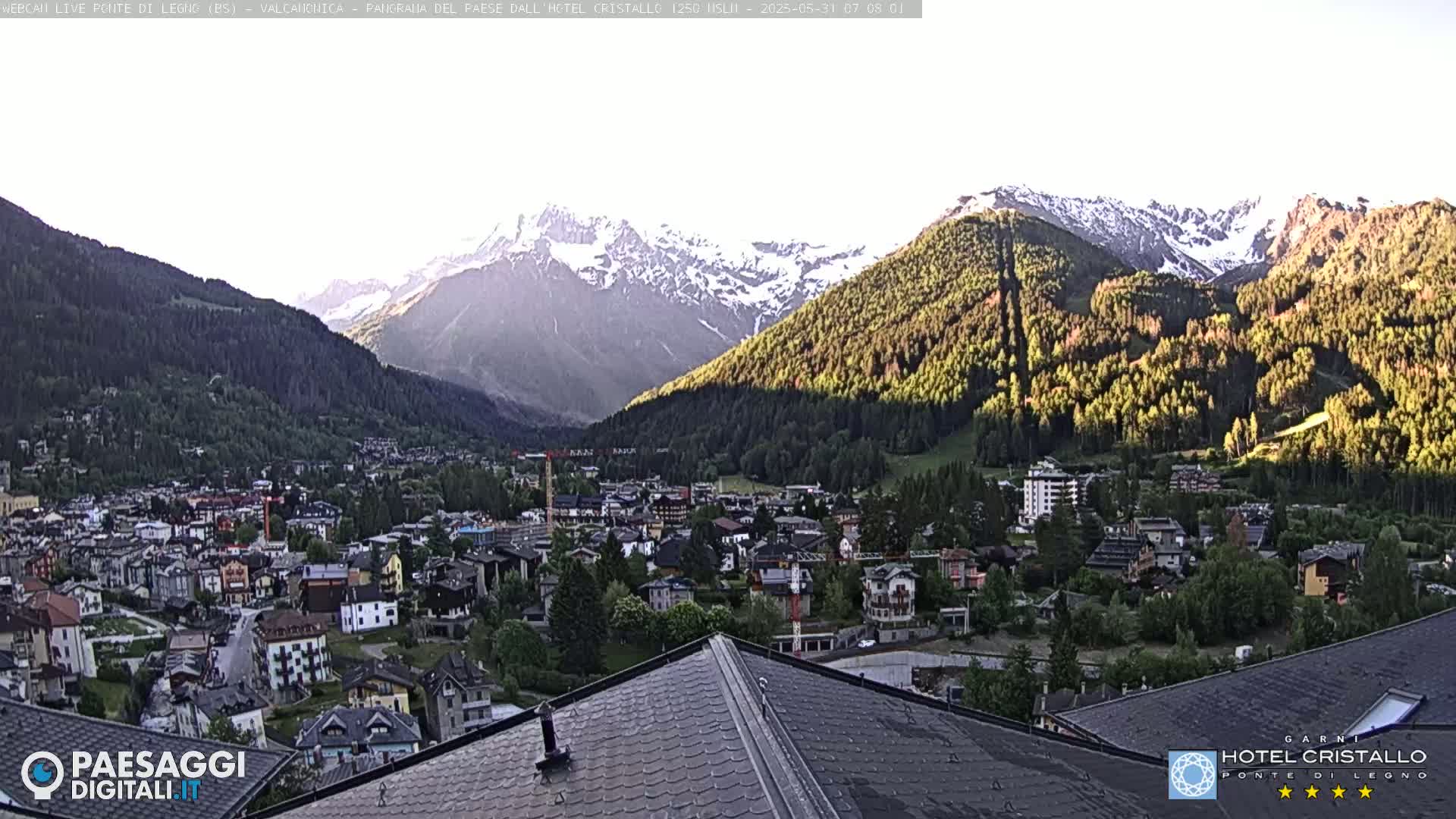 A mountain town nestled in a valley, with snow-capped mountains in the background, under a clear, bright sky.