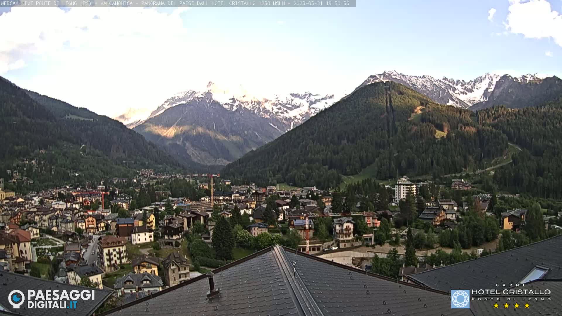 A mountain town nestled in a valley, with snow-capped mountains in the background under a mostly clear sky.