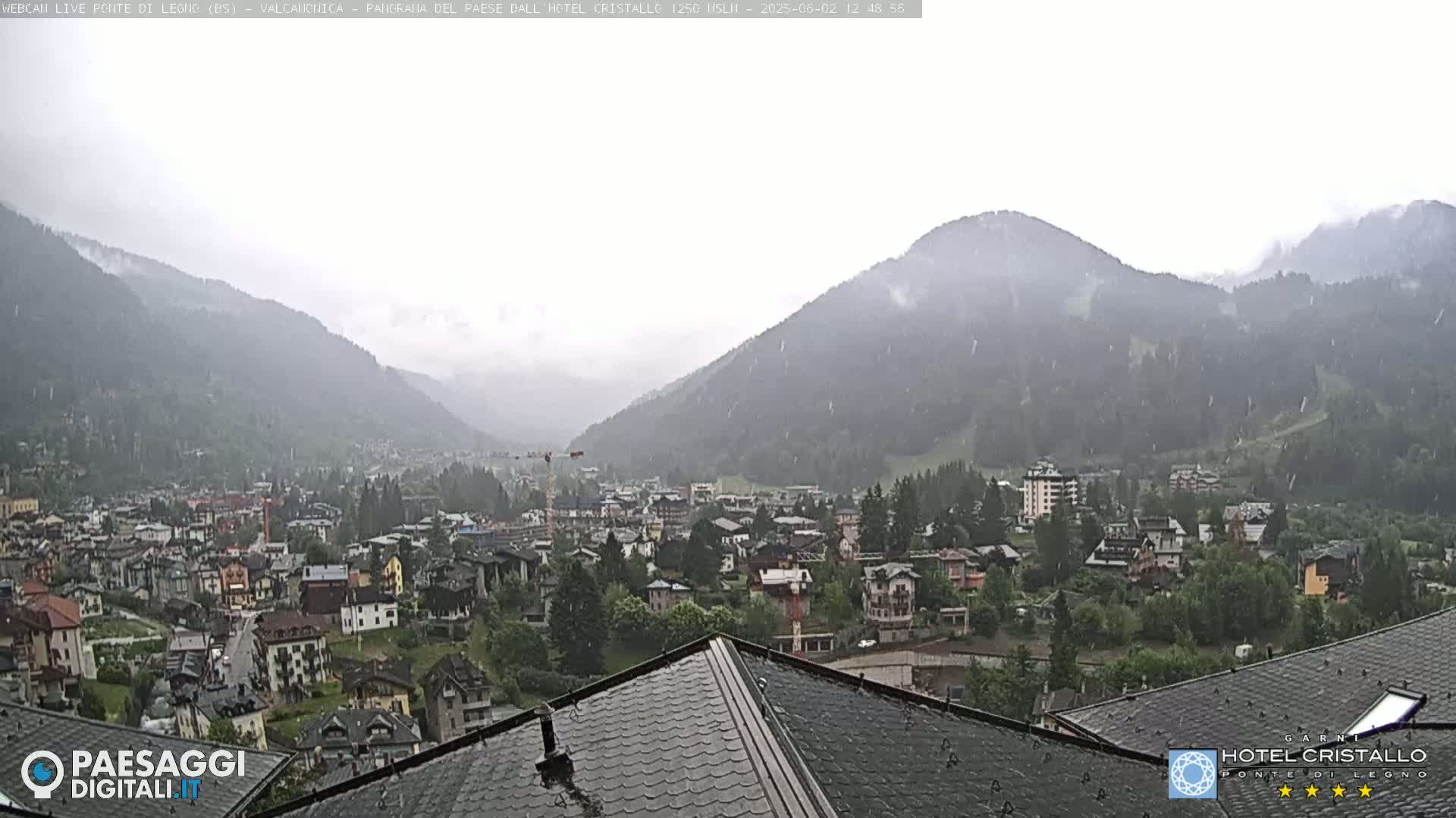 A town nestled in a valley between mountains is experiencing light rain or snow.