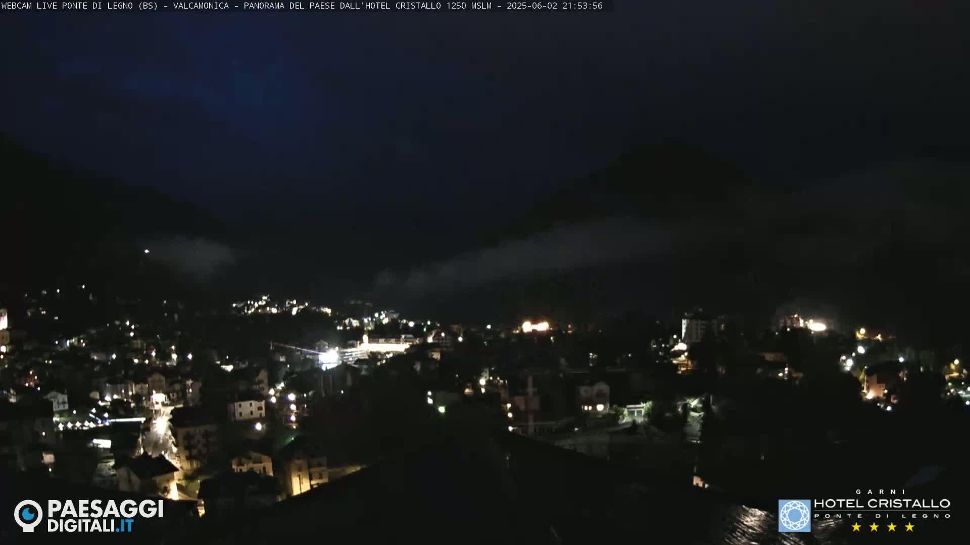 A nighttime view of a town nestled in a valley, partially obscured by fog or low clouds.