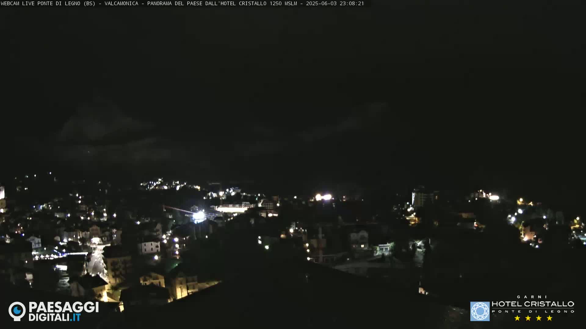 A nighttime, high-angle view of a town with scattered lights under a dark, cloudy sky.