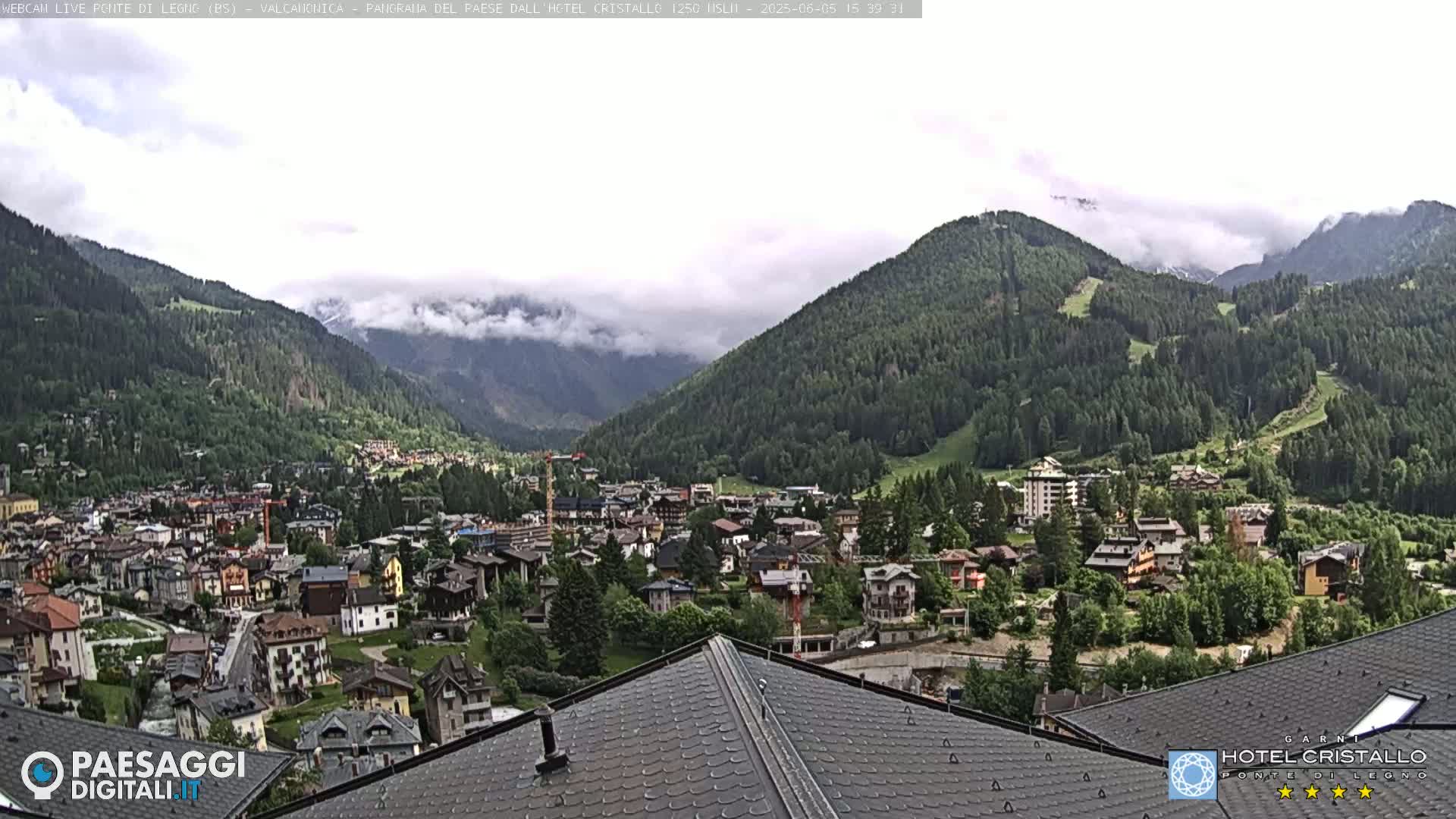 A mountain town nestled in a valley between green, tree-covered hills, partially obscured by low-lying clouds.