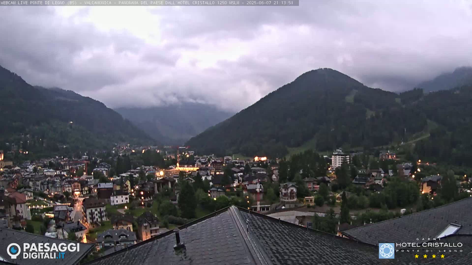 A nighttime view of a town nestled in a valley between mountains under an overcast sky.