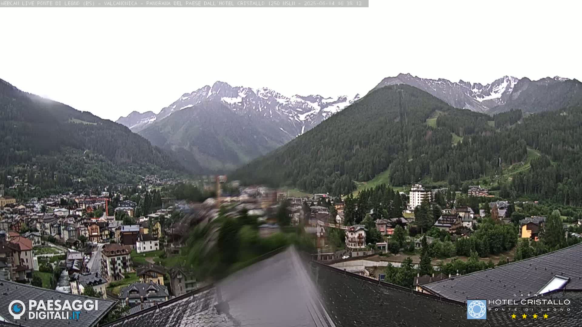 A mountain village nestled in a valley, overlooked by snow-capped mountains under an overcast sky.