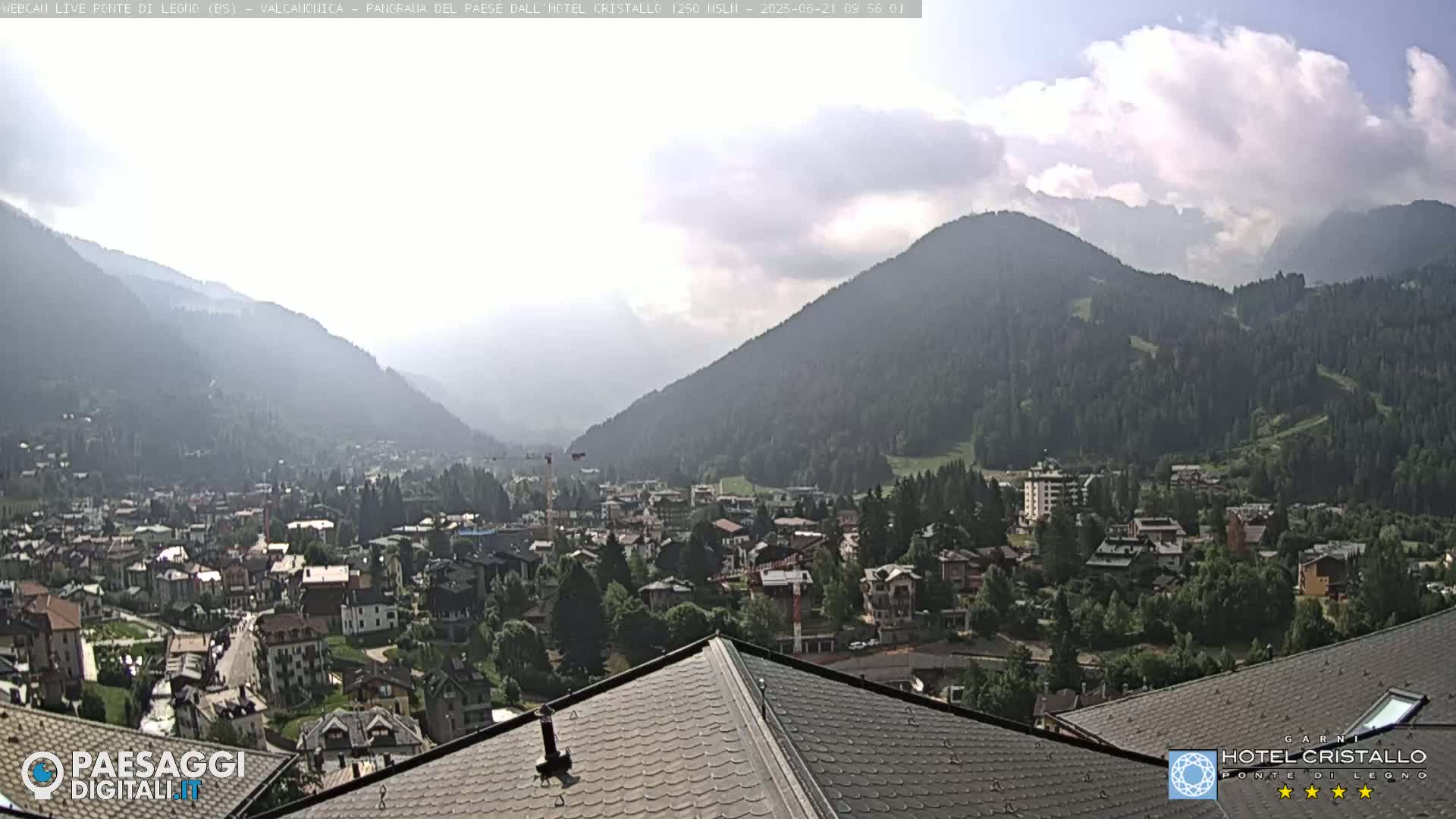 A mountain town nestled in a valley, partially obscured by a hazy sky, is seen from a rooftop.