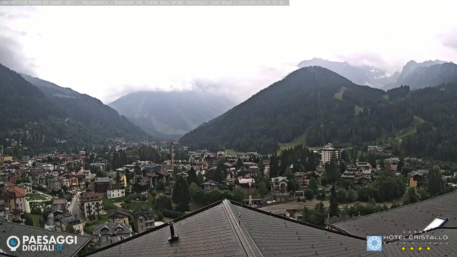 A mountain town nestled in a valley under a cloudy sky, viewed from a rooftop.