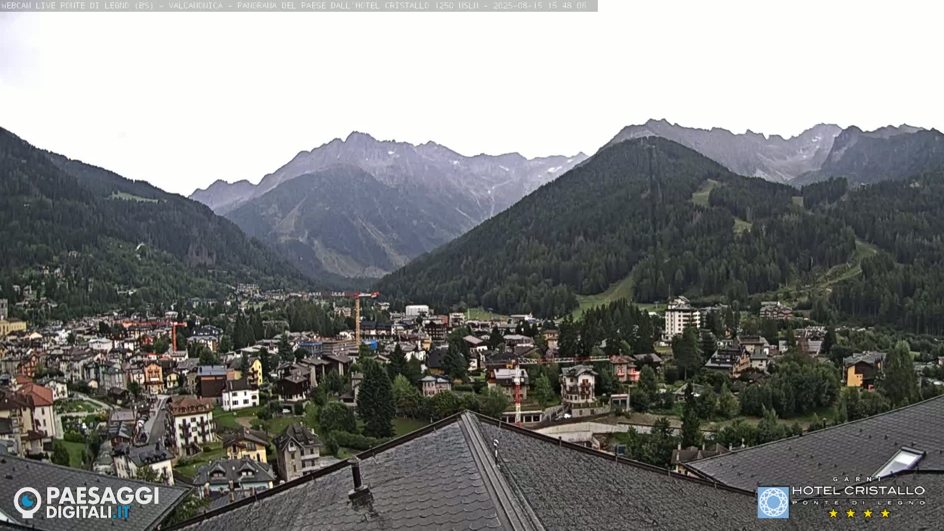 A mountain valley town is viewed from a rooftop on a sunny day, with a range of mountains in the background.