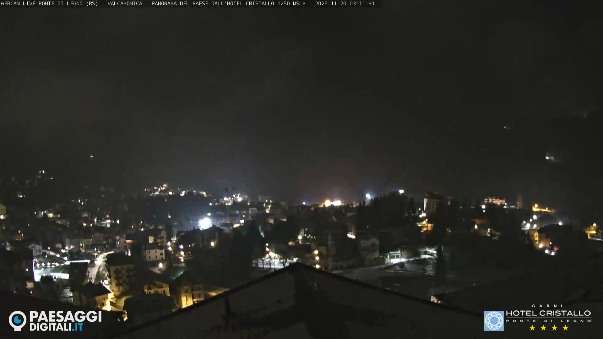 A panoramic nighttime view reveals a town illuminated by numerous street and building lights under a clear, dark sky.