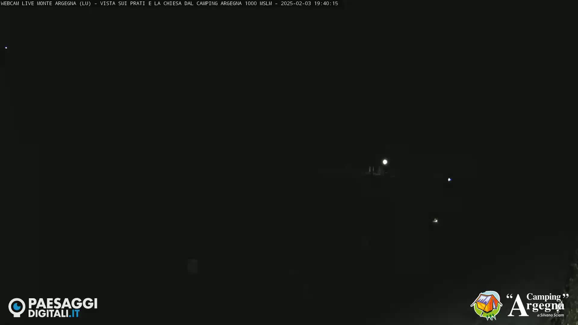 A nighttime long shot shows a dark landscape with a few faint lights visible in the distance under a moonlit sky.