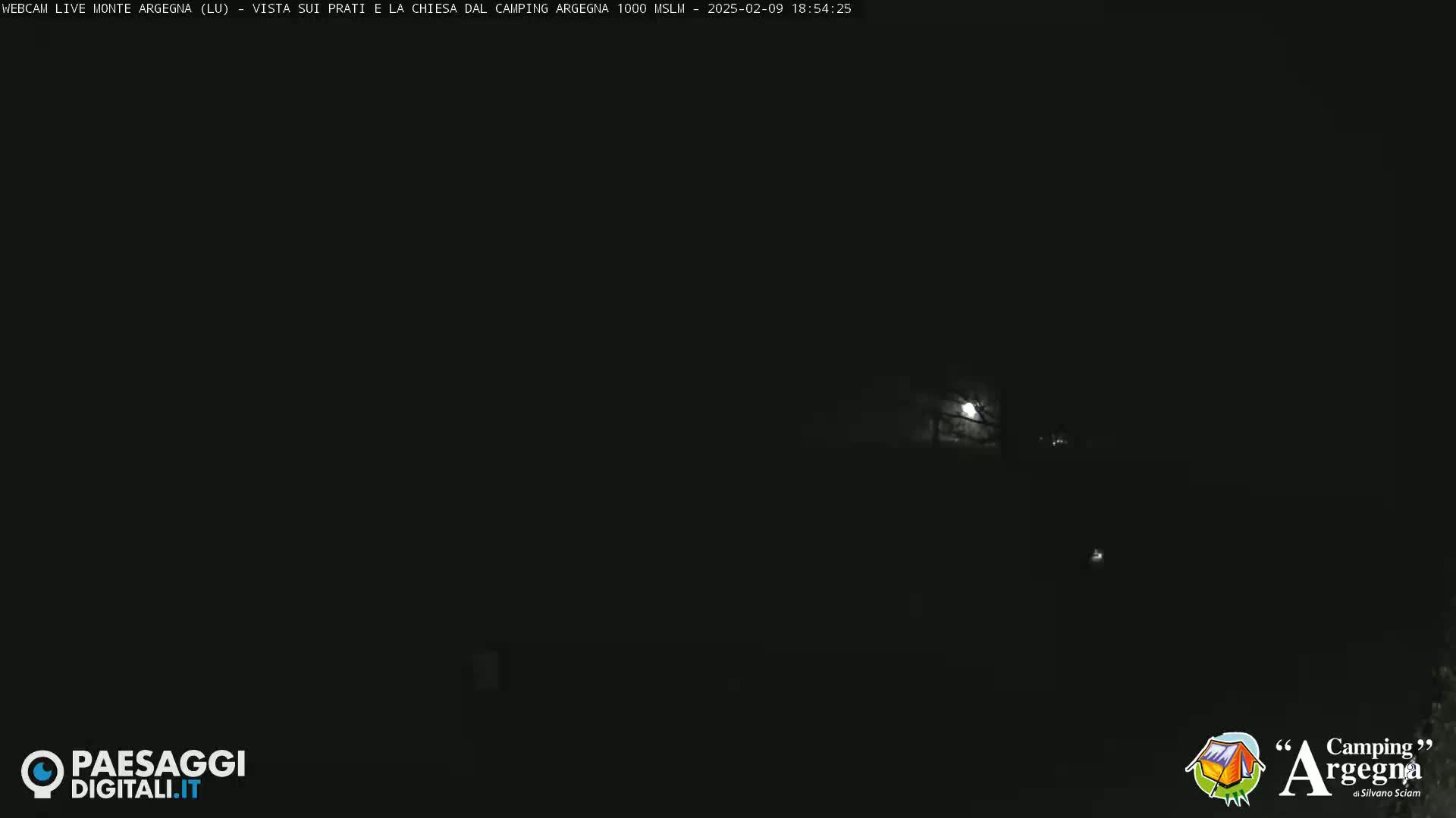 A nighttime, dark view of a landscape with a single light source visible in the distance.