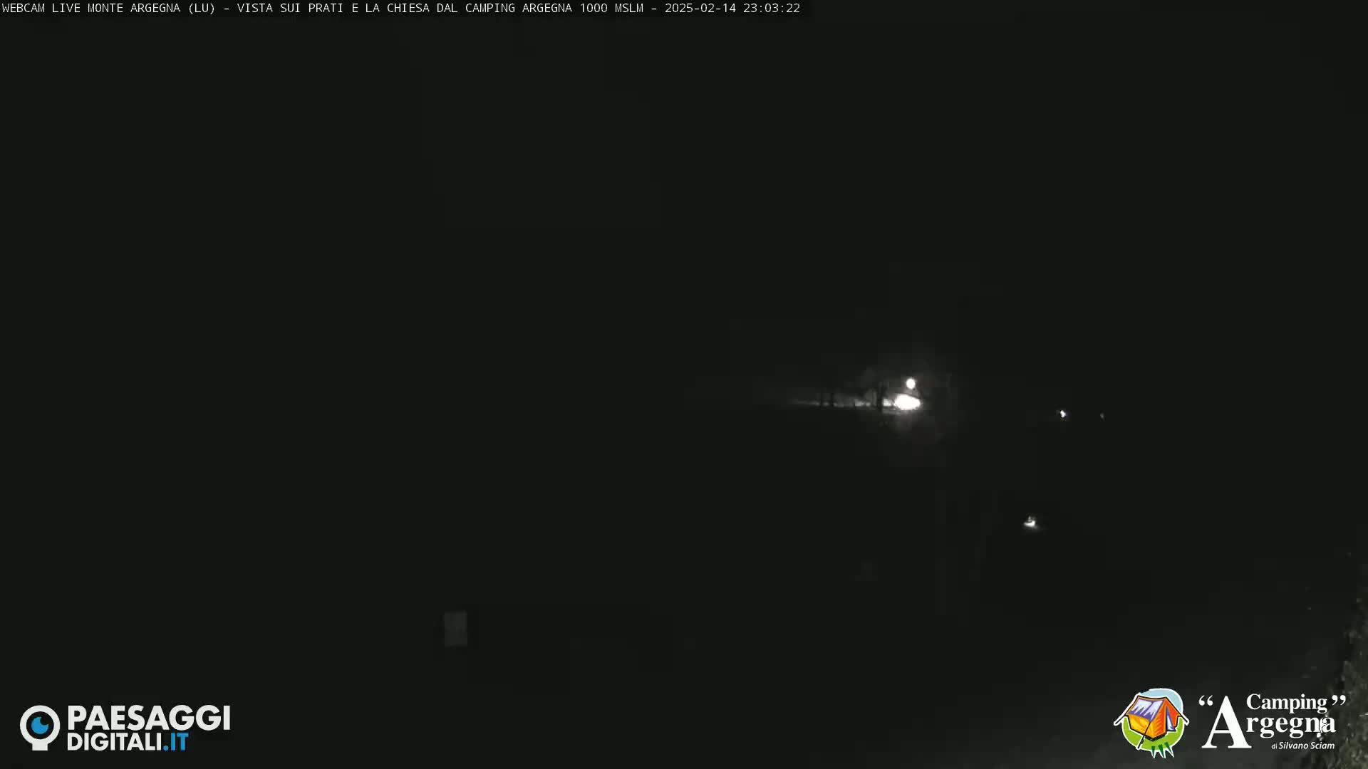 A dark, nighttime scene shows a dimly lit road or path with faint lights in the distance.