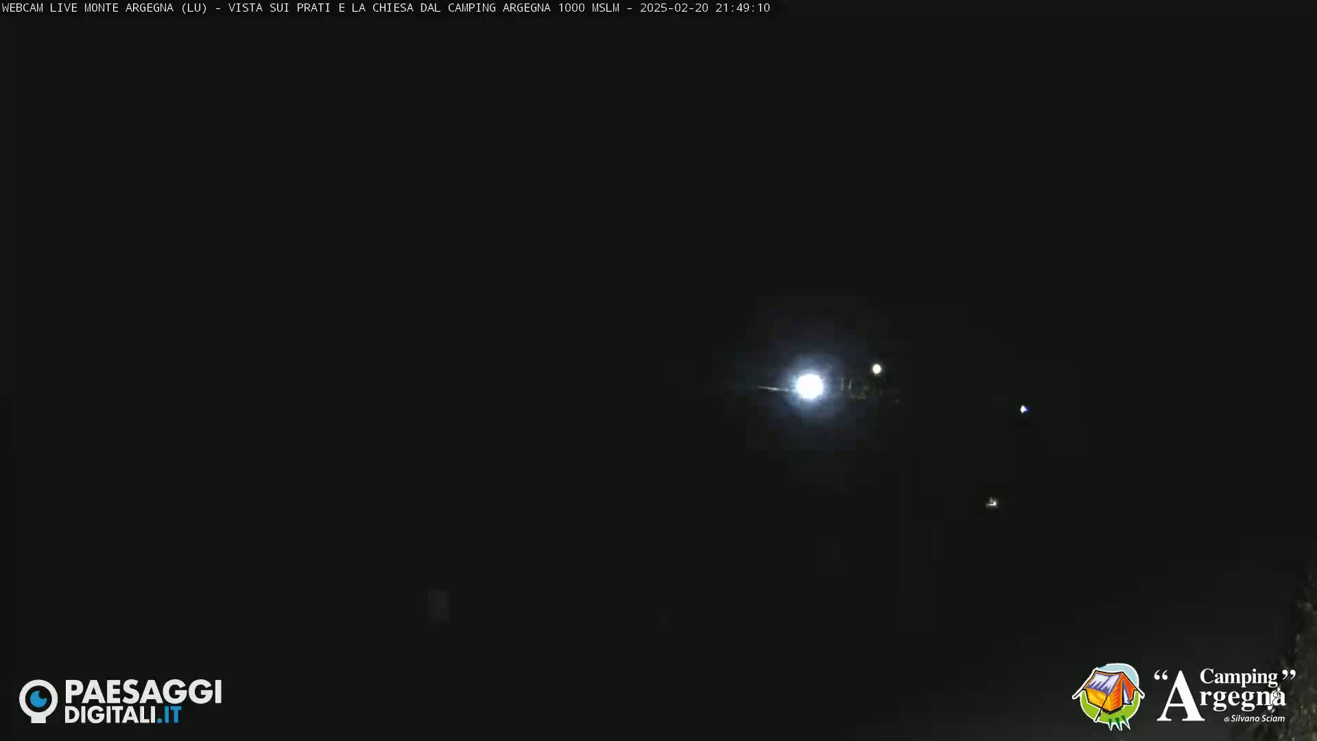 A nighttime, dark scene shows distant lights against a completely black sky.