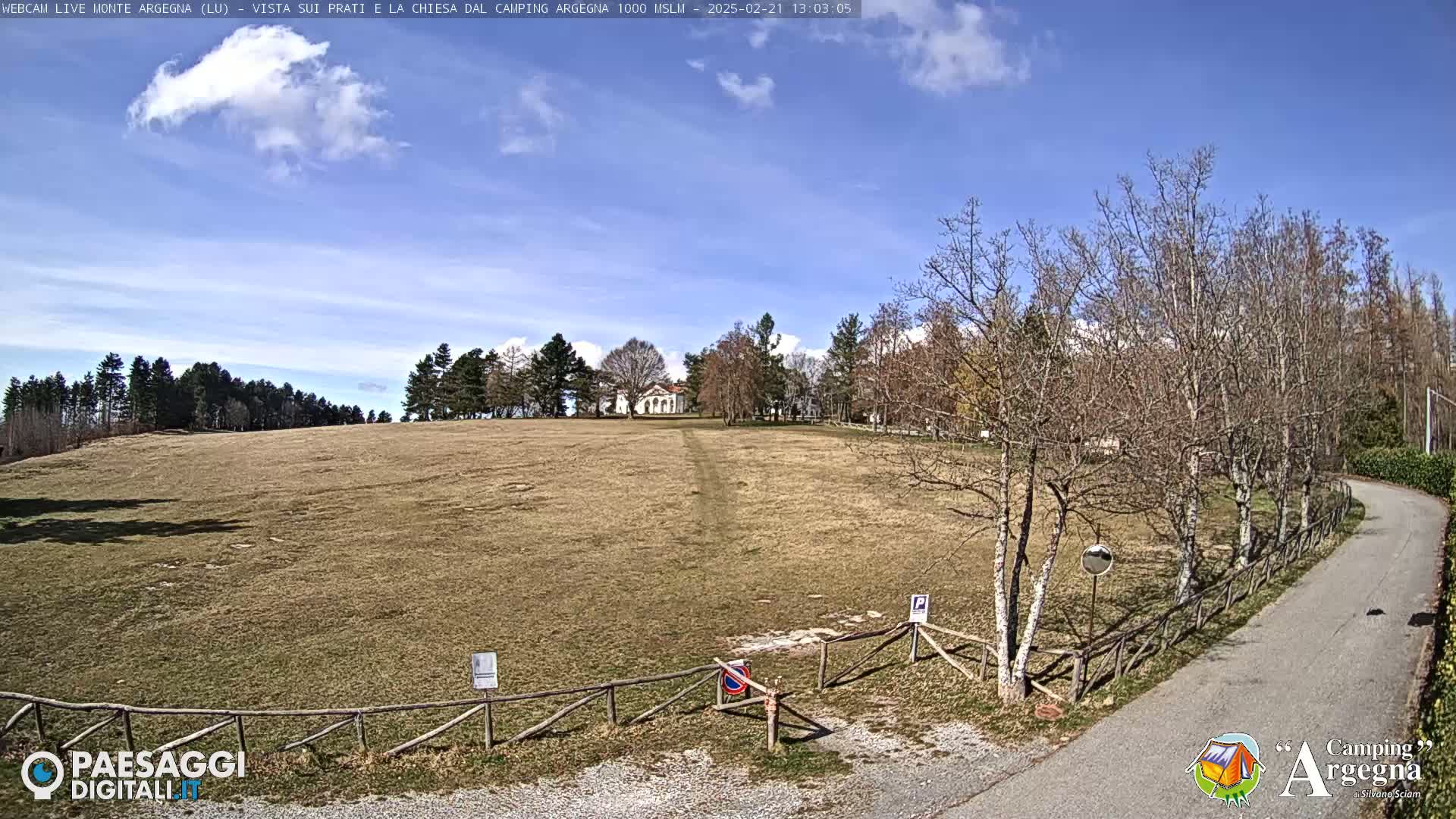 A mostly barren, tan-colored field stretches toward a small white building under a mostly clear, light-blue sky.
