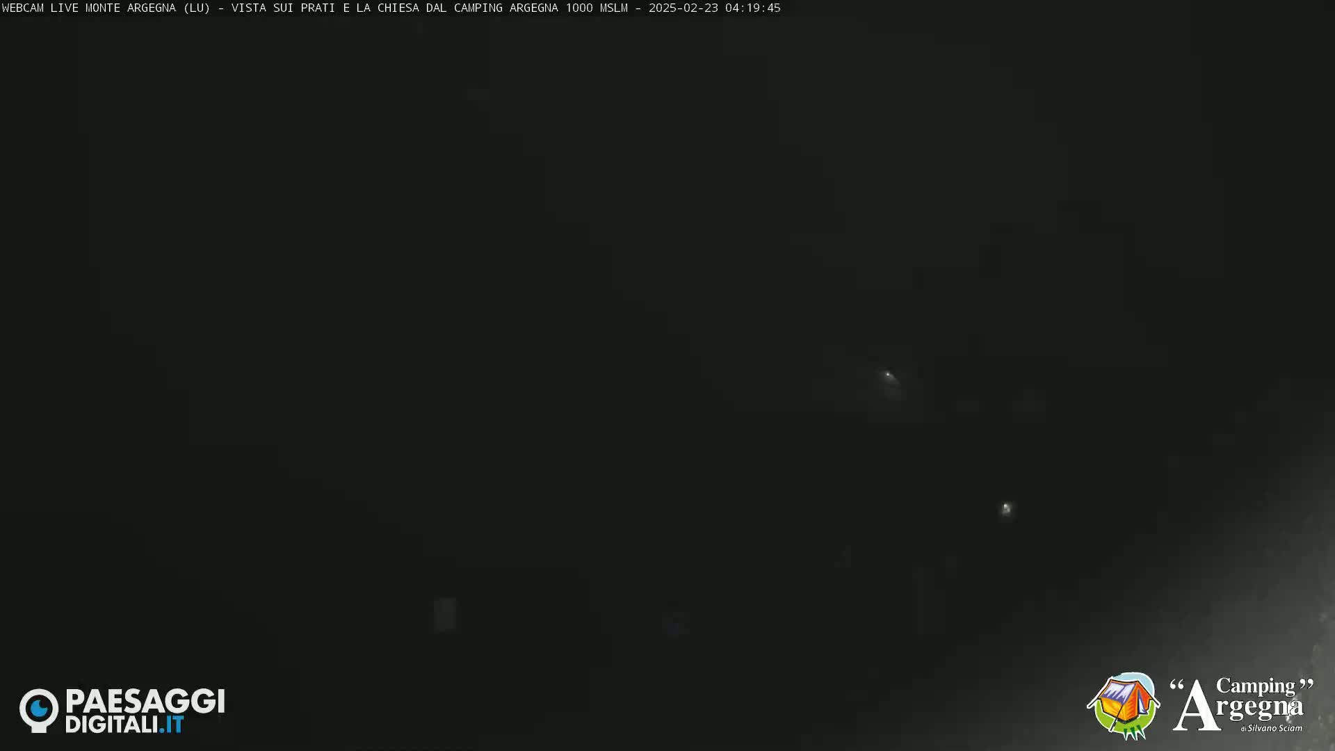 A very dark, nighttime image shows a few faint lights in the distance.