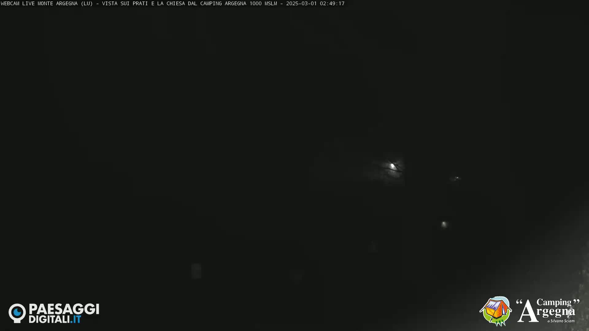 A nighttime long shot shows a dark, possibly overcast sky illuminated by a few distant lights.