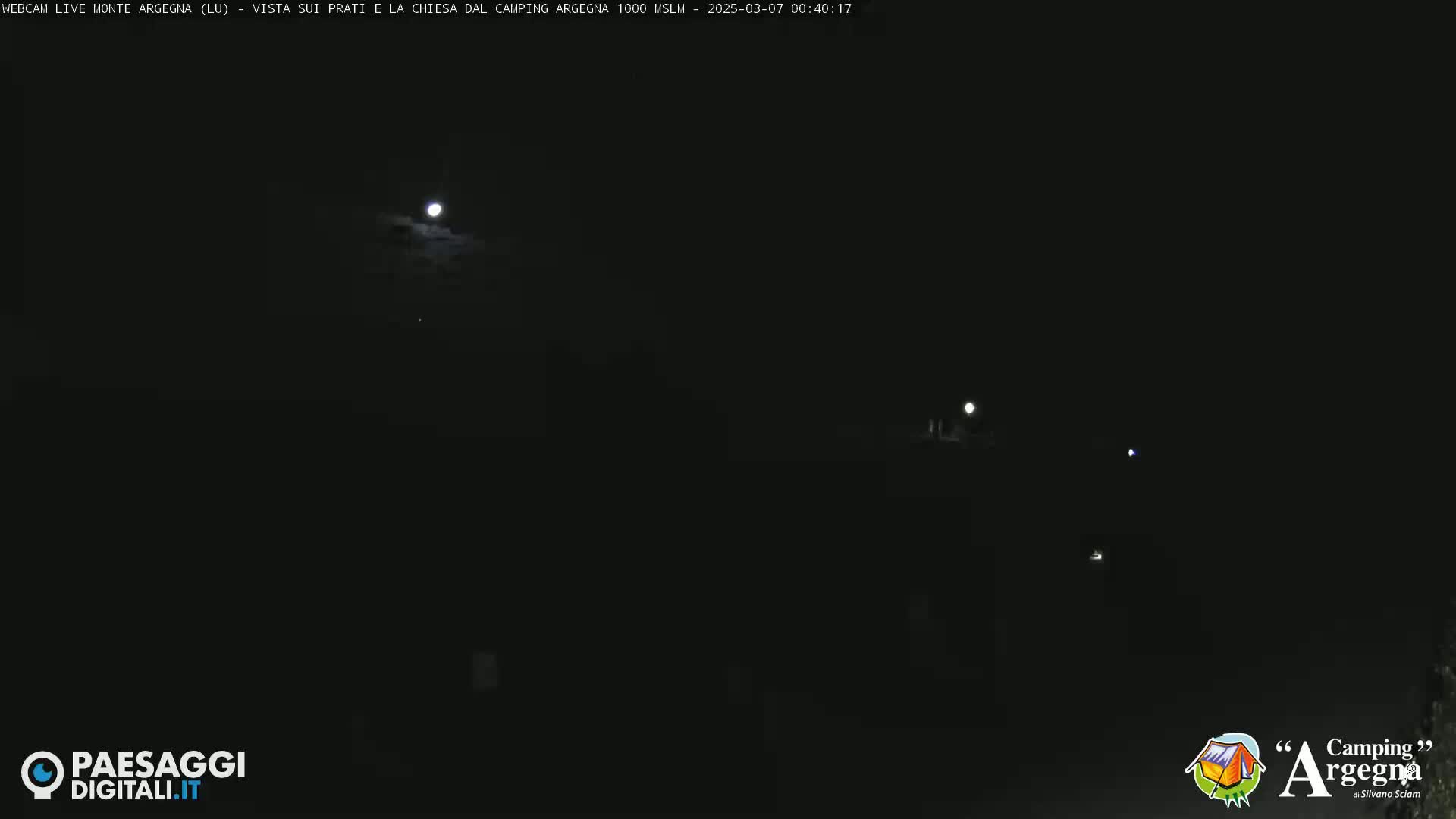 A bright moon shines in a dark, nighttime sky above a dimly lit landscape.