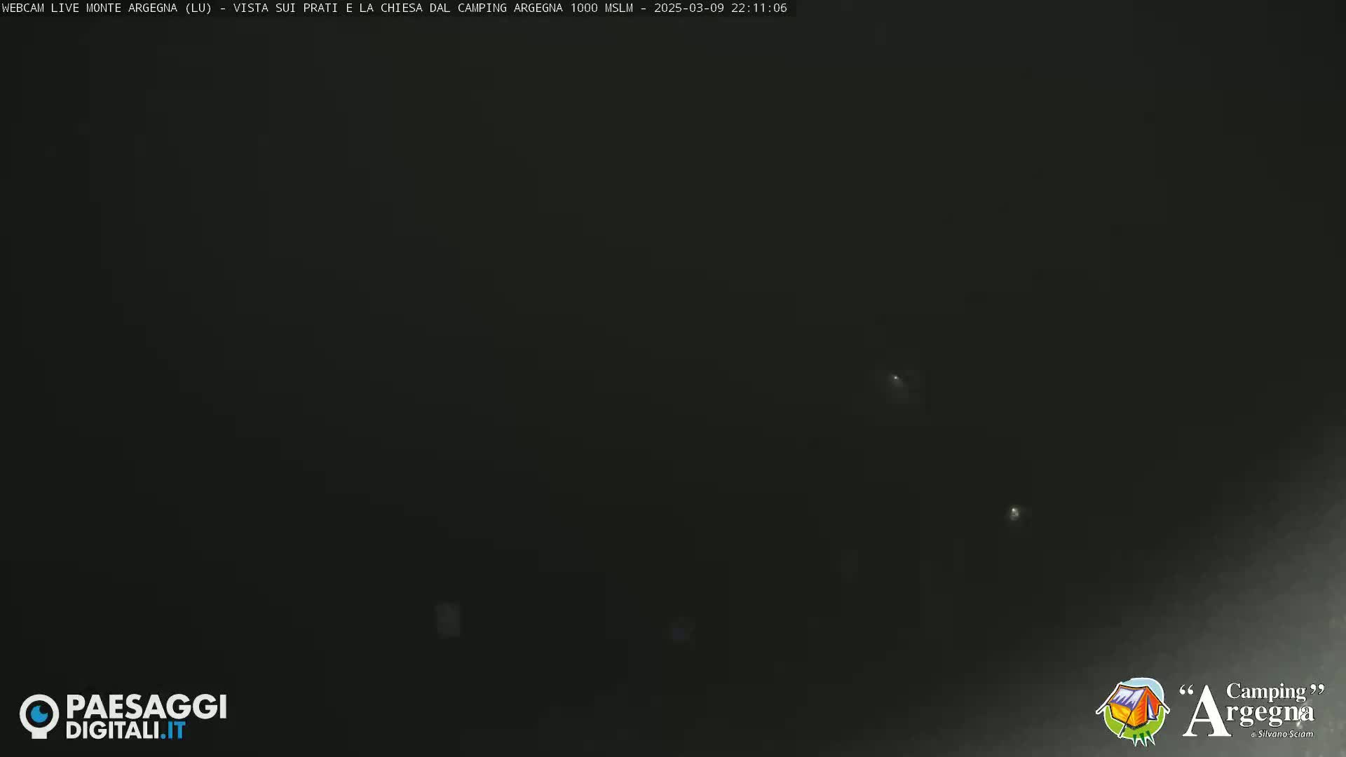 A dark, nighttime scene shows a few faint lights in the distance.