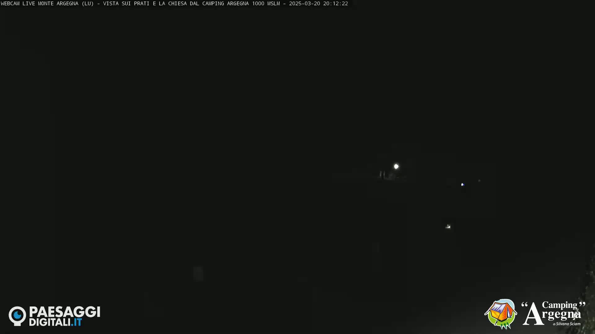 A nighttime, dark scene shows a few faint lights in the distance.