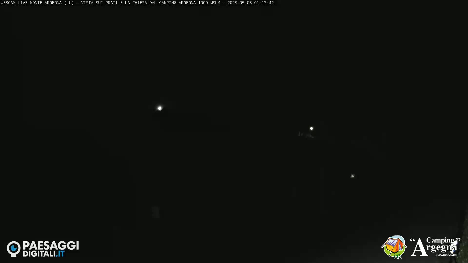 A dark, nighttime scene shows several faint lights in the distance.