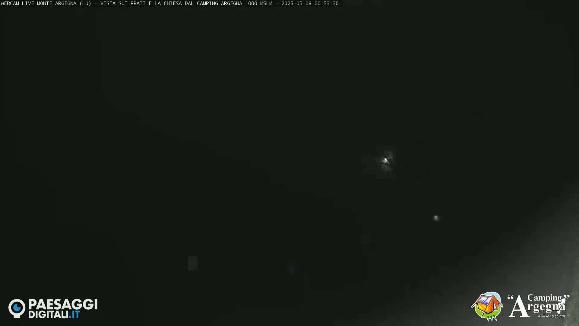 A dark nighttime scene shows a few faint lights in the distance under a mostly clear sky.