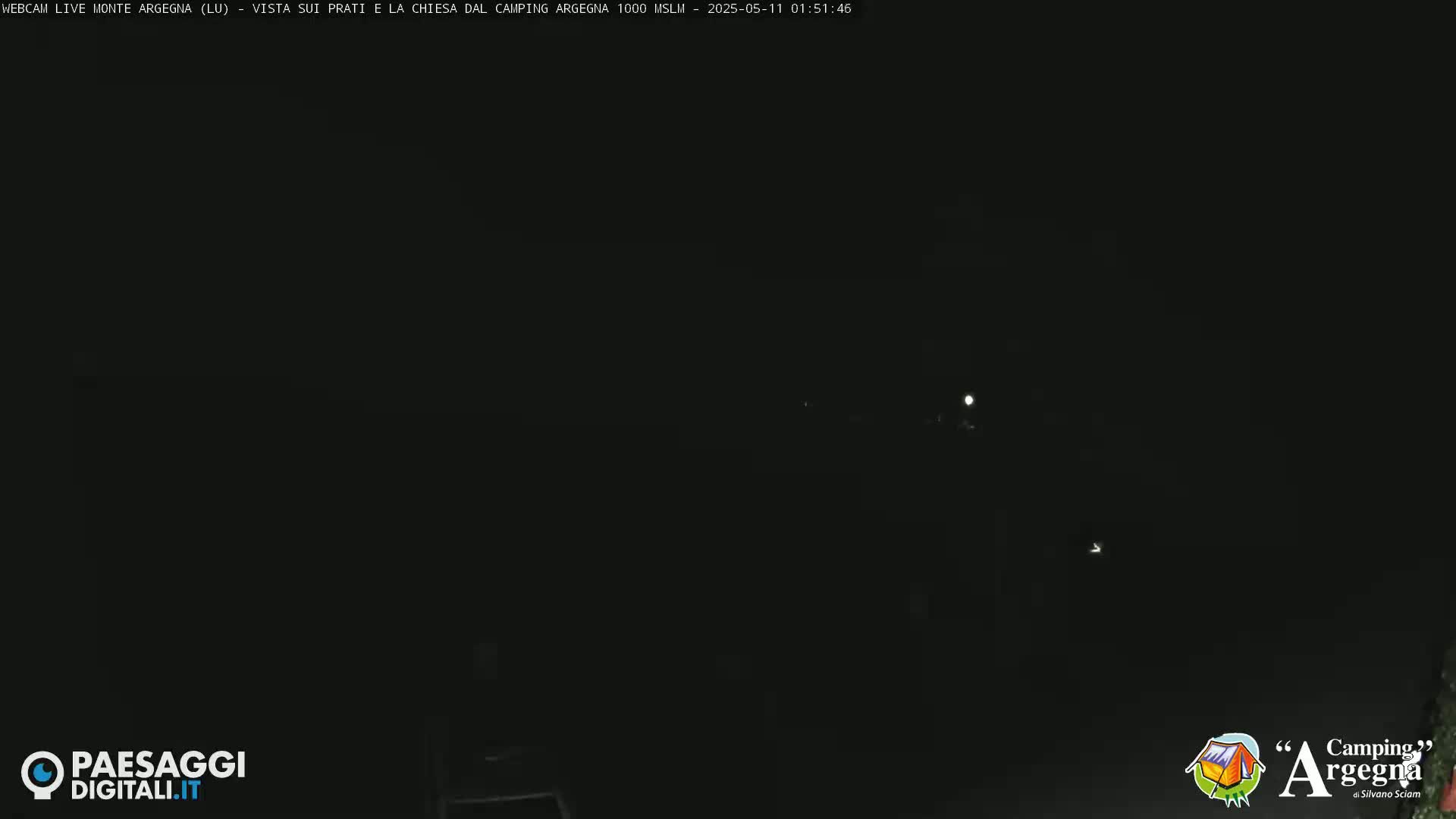 A nighttime, dark scene shows a few faint lights in the distance under a clear, moonlit sky.
