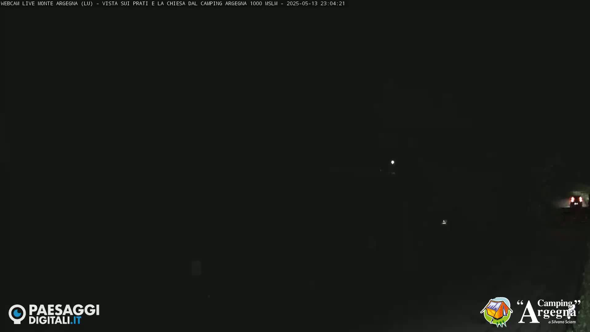 A dark, nighttime scene shows a few distant lights and a vehicle's taillights in the lower right corner.