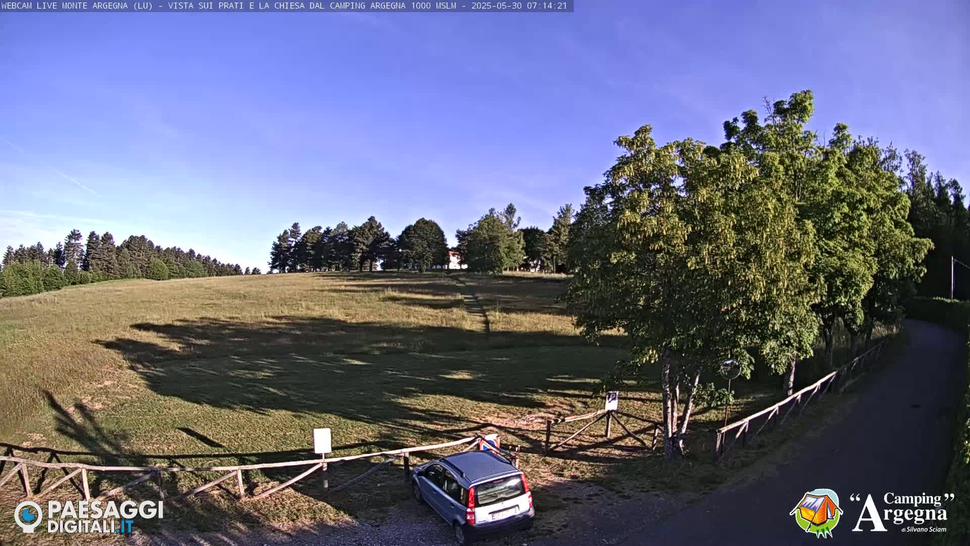A grassy field with a few trees and a small car is visible under a clear blue sky.