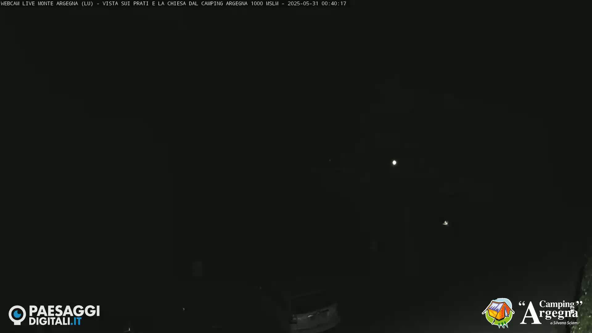 A nighttime, dark scene shows a few faint lights in the distance under a clear, moonlit sky.