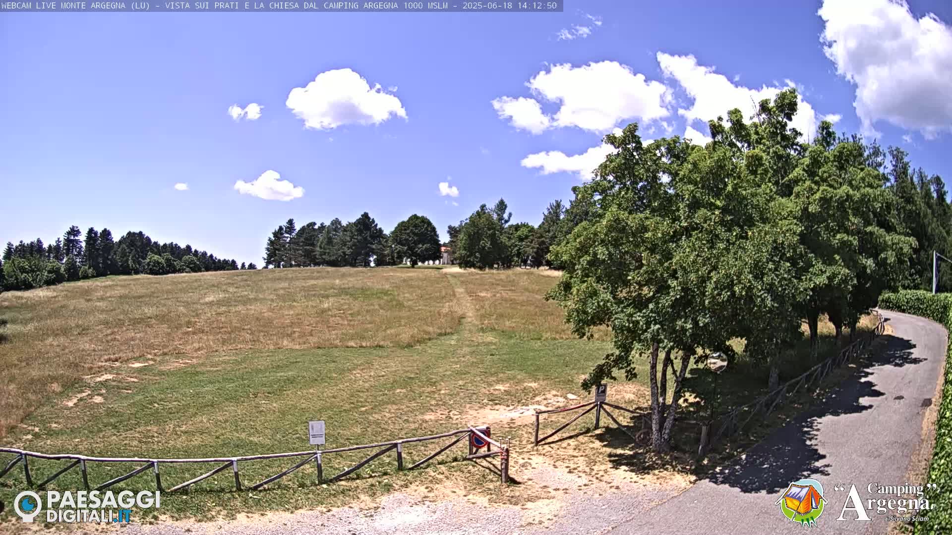 A grassy field with a dirt path leading to a building in the distance under a partly sunny sky.