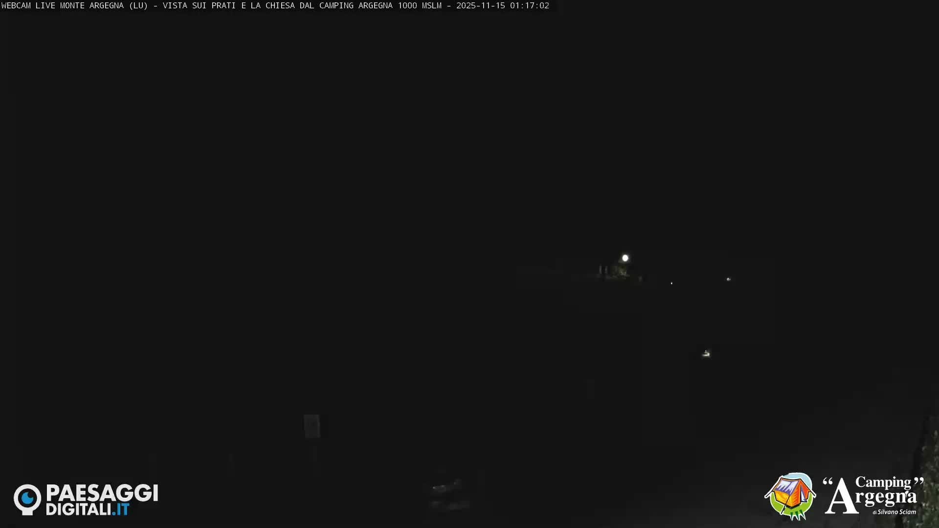 The image displays an extremely dark outdoor nighttime scene, with a few faint lights scattered in the distance under clear conditions.