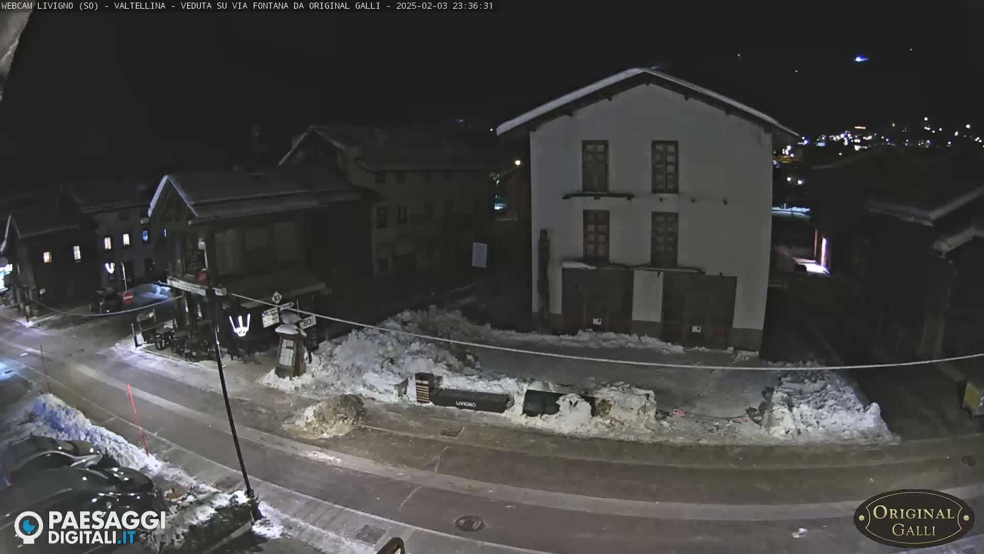 A nighttime street scene in a snow-covered village shows several buildings under a dark sky.