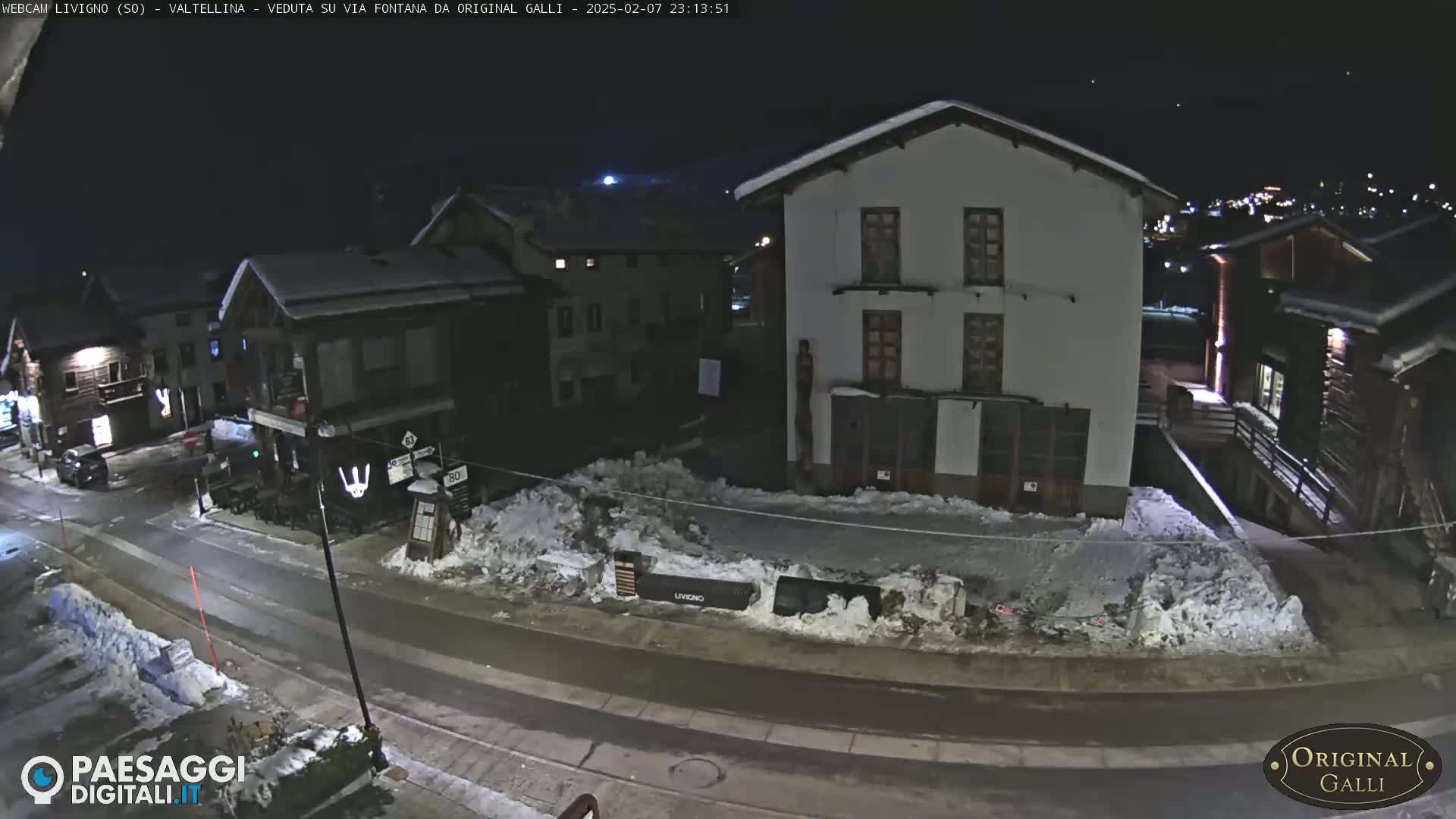 A snow-covered street at night in a village, lined with buildings, some of which are lit.