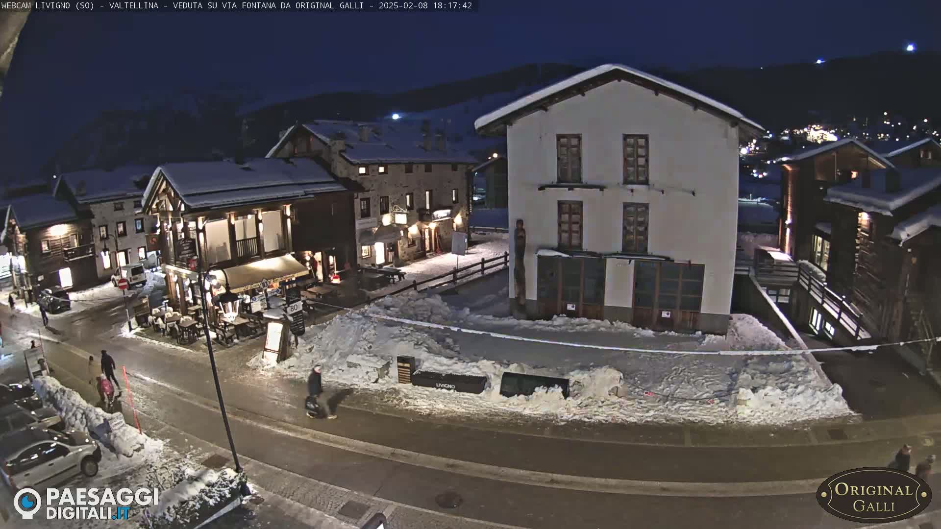 A snow-covered village street at night, with several buildings and a few pedestrians.