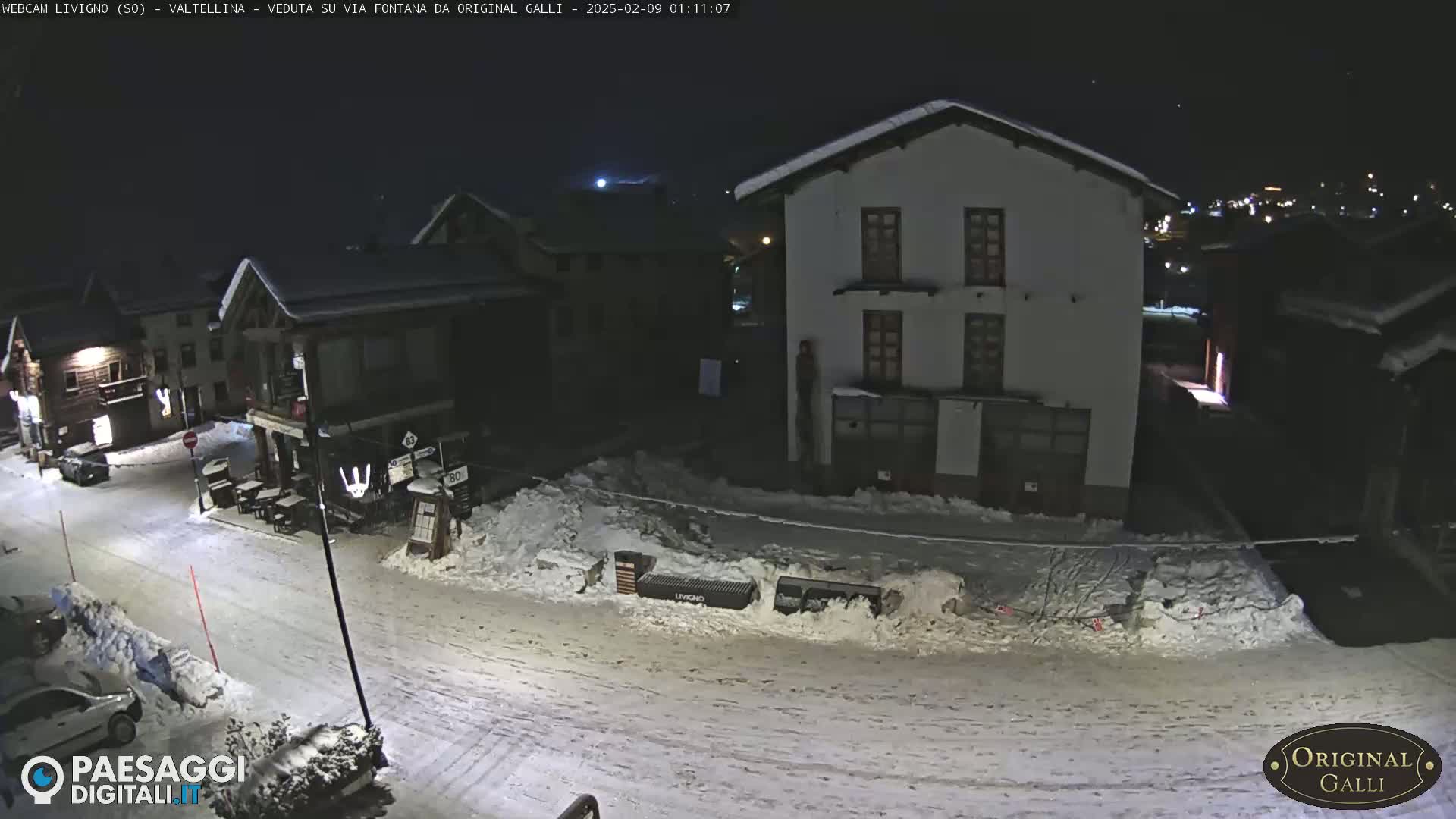 A snow-covered street at night in a village, with several buildings illuminated.
