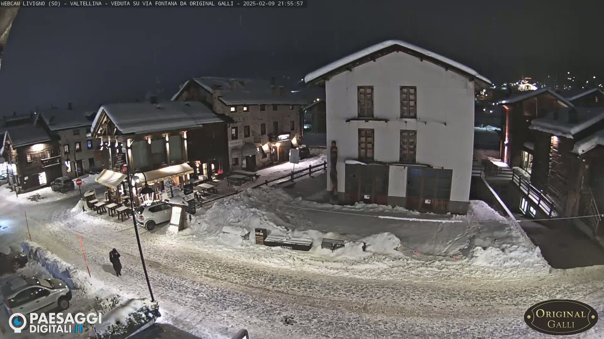 A snow-covered village street at night, with several buildings illuminated, is visible under a dark sky.