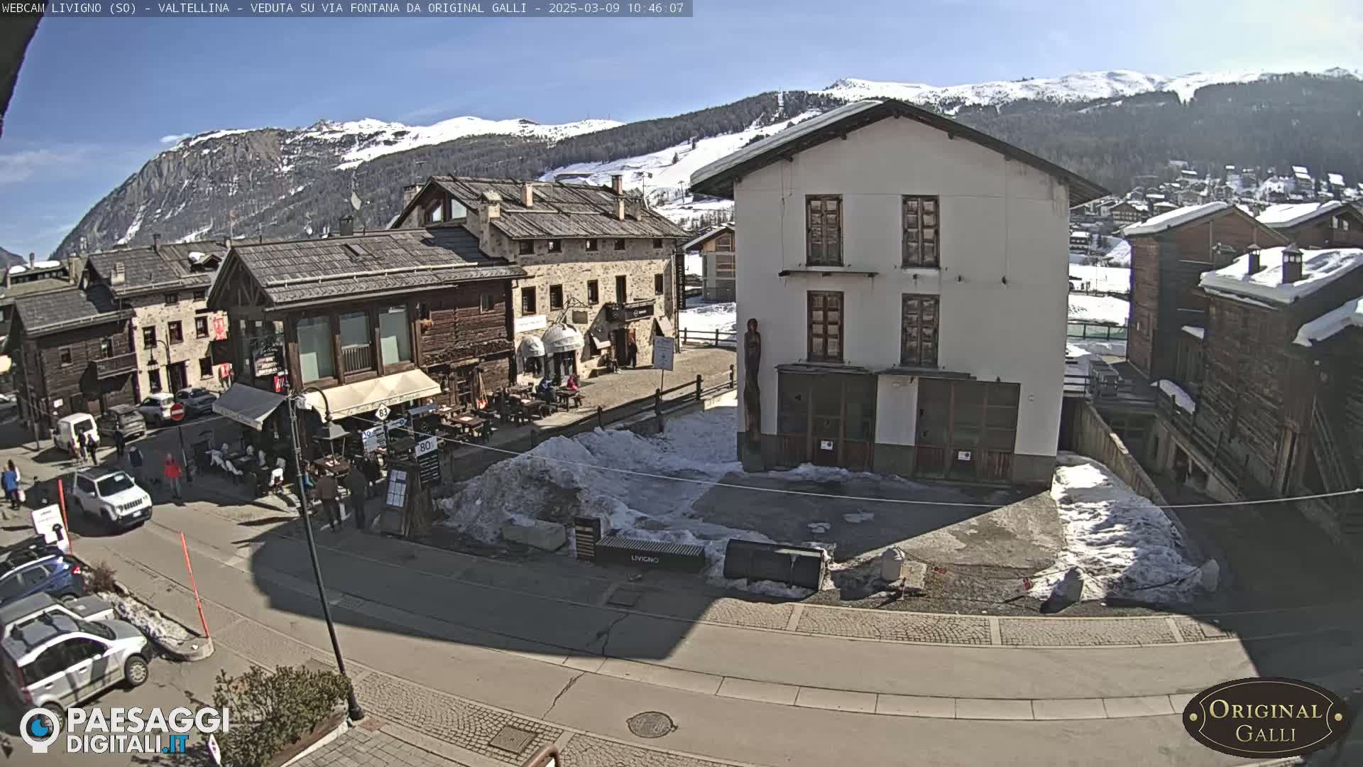A sunny day in a snow-dusted village nestled in a valley, surrounded by snow-capped mountains.