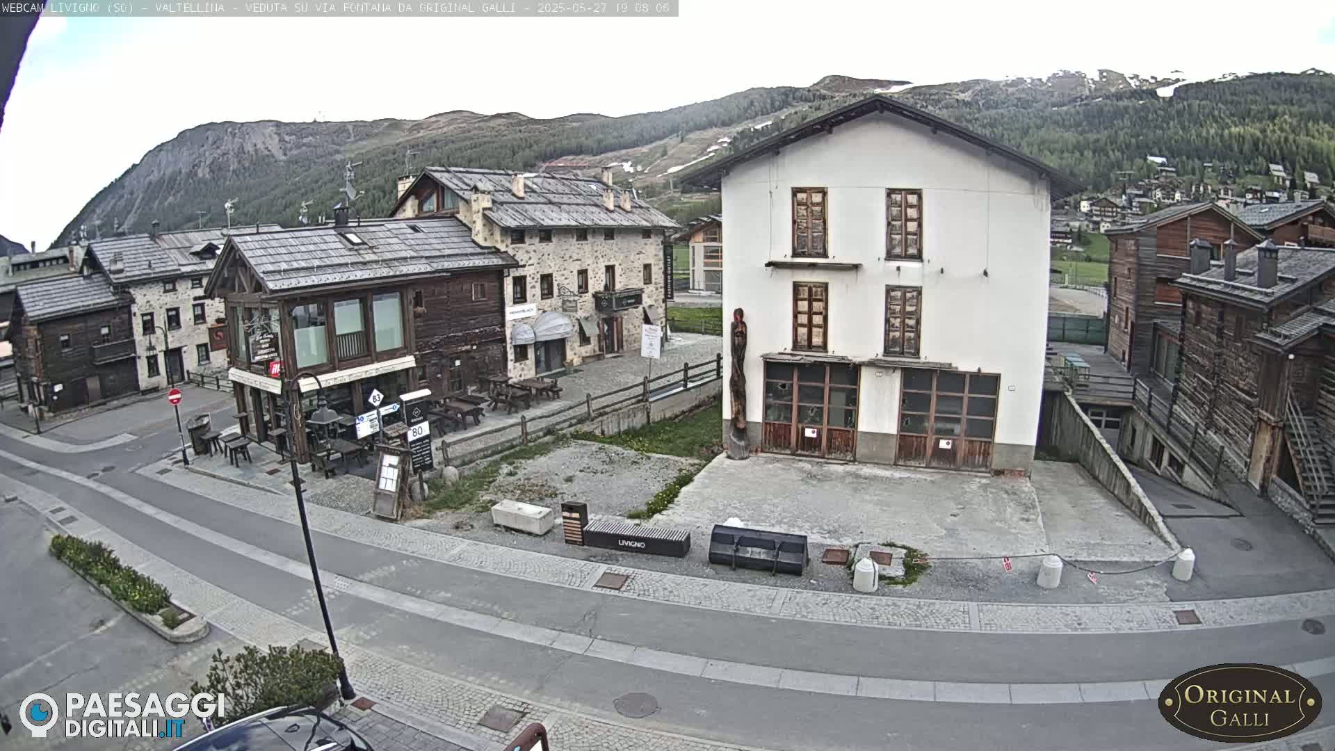 A mostly cloudy day in a small mountain village with several buildings of varying architectural styles situated around a paved road.