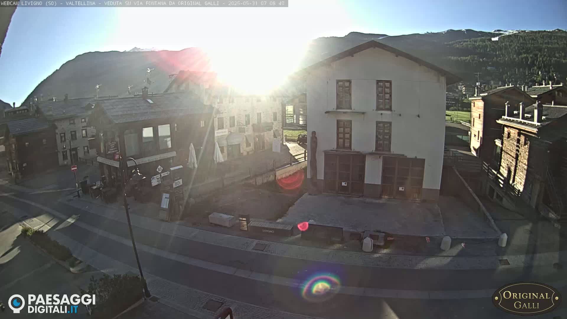 A sunlit view of a village street nestled in a mountain valley on a clear morning.