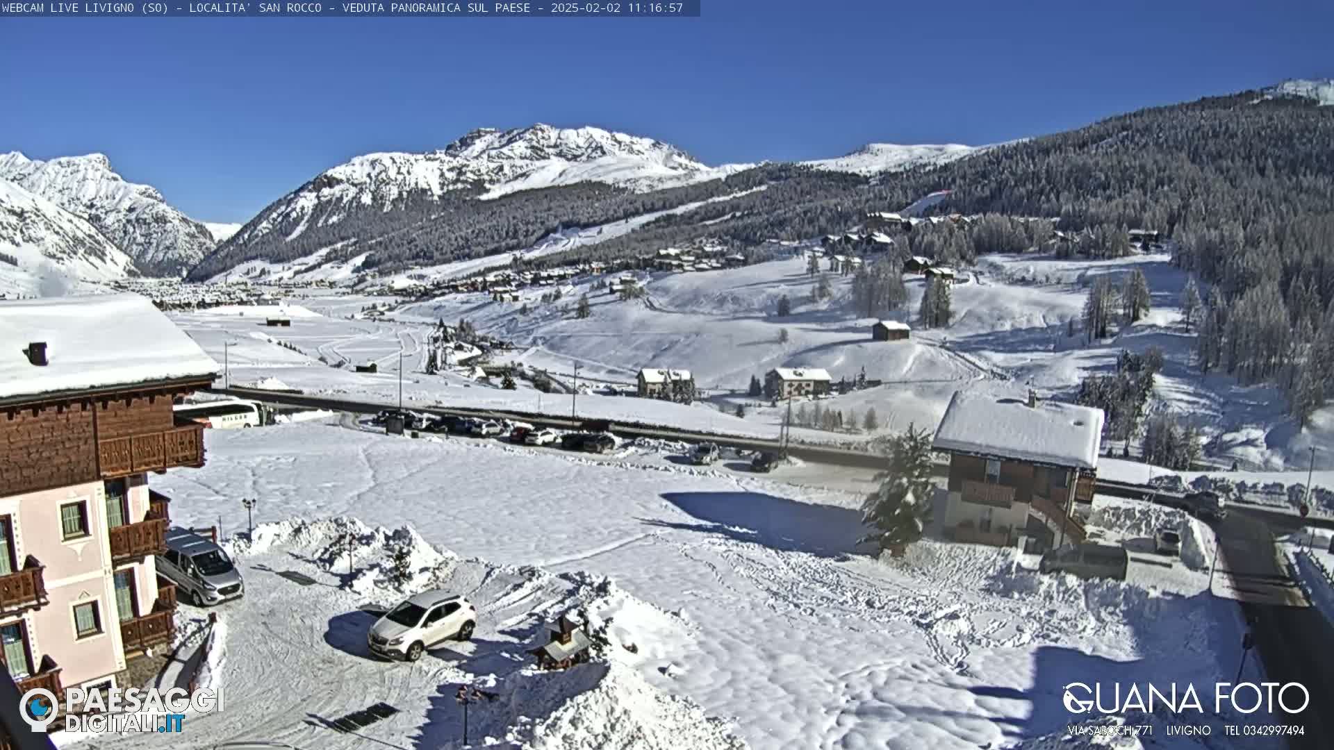 A snow-covered mountain village scene is visible under a clear blue sky, with cars parked in a snow-covered lot in the foreground.