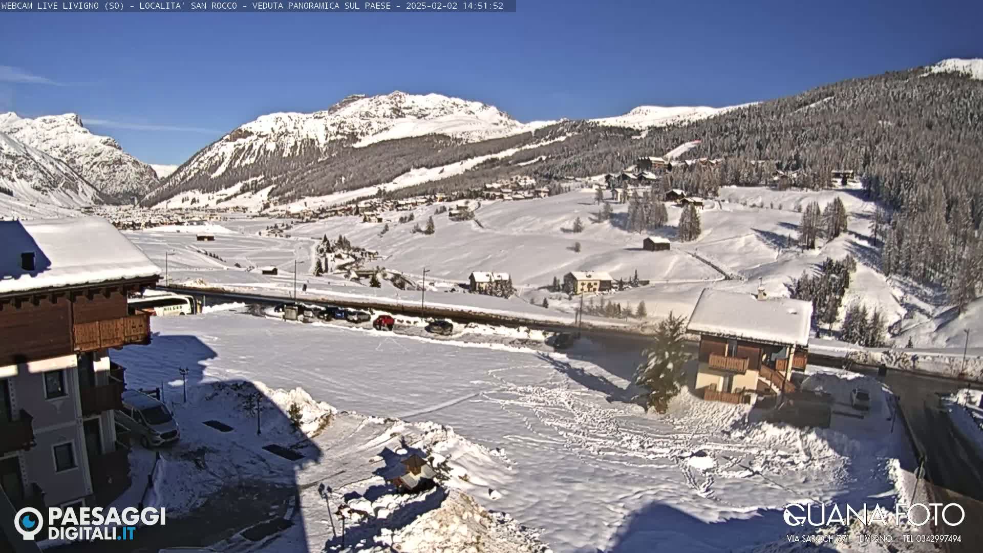 A snow-covered village nestled in a valley between snow-capped mountains on a sunny day.