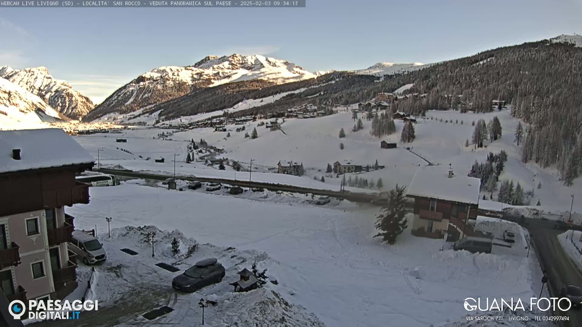 A snow-covered mountain village is seen from a high vantage point on a clear, sunny day.